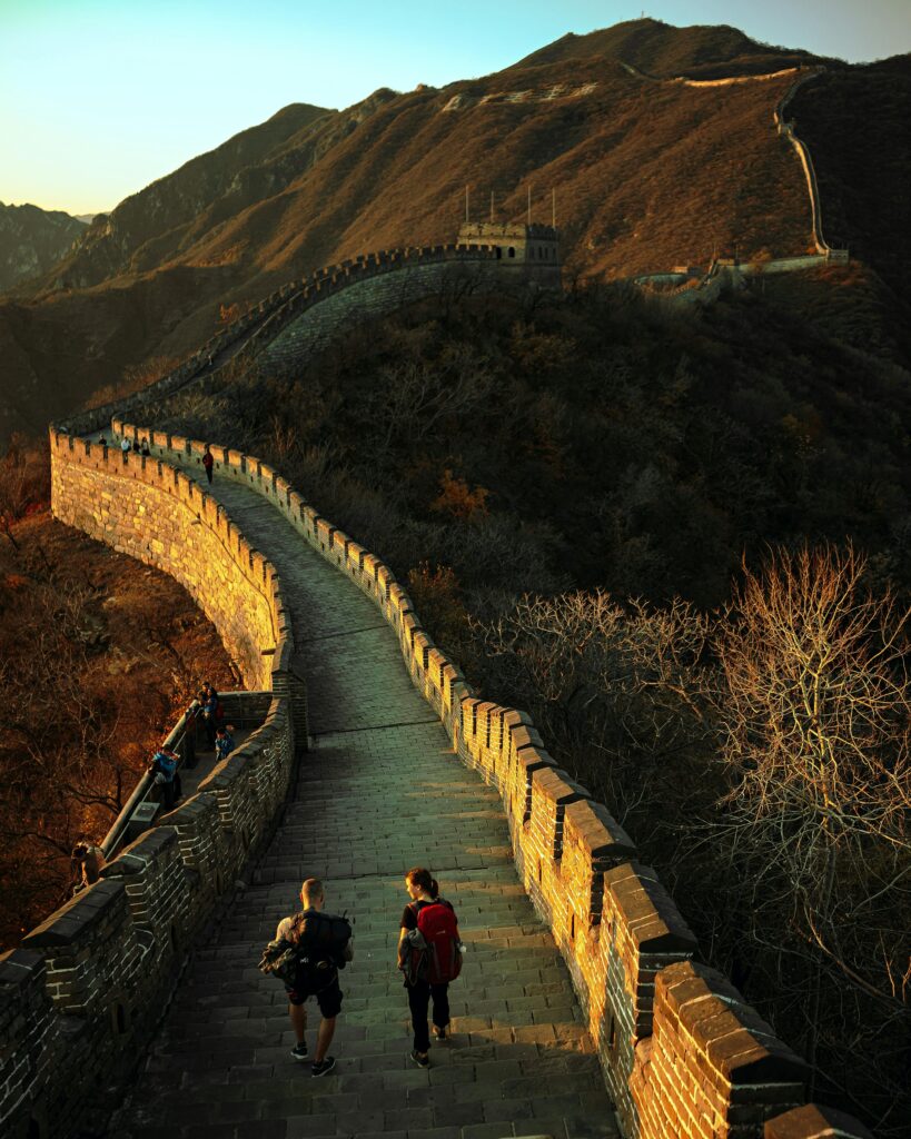 Tourists walking along the Great Wall of China at sunset with mountainous backdrop.